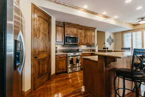 Kitchen featuring appliances with stainless steel finishes, a breakfast bar area, dark wood finished floors, crown molding, and brown cabinets