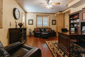 Home office featuring a ceiling fan, dark wood-style flooring, crown molding, and a fireplace