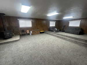 Basement featuring a wood stove, a textured ceiling, wooden walls, and carpet floors