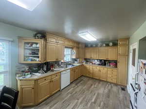 Kitchen featuring light brown cabinets, light countertops, light wood-type flooring, white appliances, and decorative backsplash