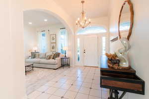 Entryway with arched walkways, ornamental molding, a chandelier, and light tile patterned floors