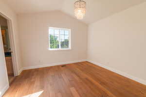 Unfurnished room with a chandelier, light wood finished floors, and vaulted ceiling