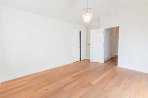 Spare room with a chandelier, light wood-style flooring, and high vaulted ceiling