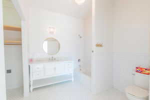 Bathroom featuring tile walls, vanity,  shower combination, tile patterned flooring, and a wainscoted wall