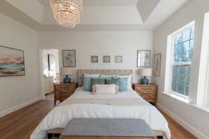 Bedroom featuring wood finished floors, a chandelier, multiple windows, and a tray ceiling