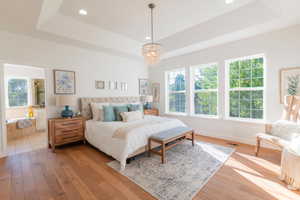 Bedroom featuring a tray ceiling, light wood-style flooring, a chandelier, recessed lighting, and ensuite bath