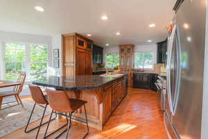 Kitchen with stainless steel appliances, recessed lighting, a center island with sink, light wood-style floors, and glass insert cabinets