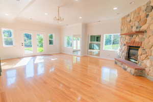 Unfurnished living room with healthy amount of natural light, a stone fireplace, light wood-type flooring, crown molding, and a chandelier