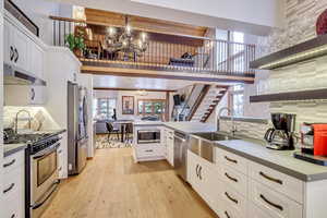 Kitchen featuring appliances with stainless steel finishes, a chandelier, light wood-style flooring, white cabinets, and backsplash
