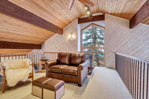 Sitting room featuring wood walls, wood ceiling, a ceiling fan, carpet flooring, and an upstairs landing