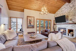 Living room featuring wooden ceiling, wood finished floors, plenty of natural light, a chandelier, and a stone fireplace