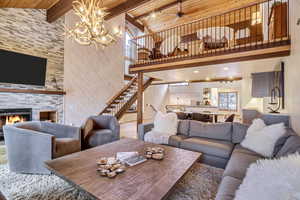 Living area featuring wood finished floors, high vaulted ceiling, a stone fireplace, stairway, and ceiling fan