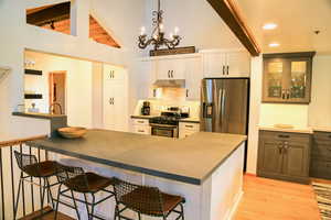 Kitchen featuring appliances with stainless steel finishes, a chandelier, backsplash, a breakfast bar area, and light wood-style flooring