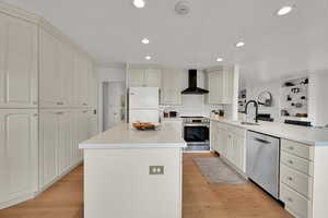 Kitchen featuring a peninsula, appliances with stainless steel finishes, wall chimney exhaust hood, a center island, and recessed lighting