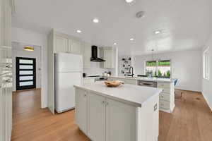 Kitchen with a peninsula, stainless steel appliances, light wood-style flooring, wall chimney range hood, and a center island