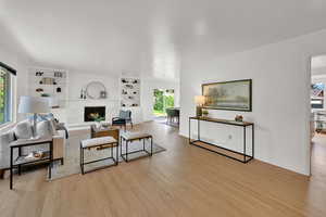 Living room with wood finished floors, a fireplace, and built in shelves