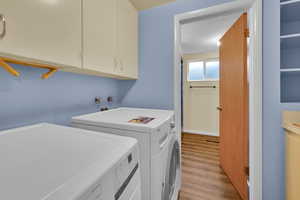 Washroom featuring washing machine and clothes dryer, light wood-style floors, and cabinet space