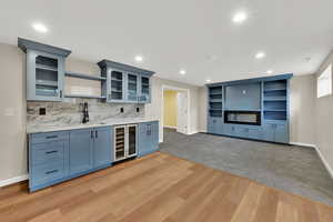 Indoor wet bar featuring beverage cooler, recessed lighting, light wood-type flooring, and decorative backsplash