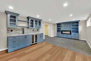 Indoor wet bar with wine cooler, recessed lighting, light wood-style flooring, decorative backsplash, and a glass covered fireplace