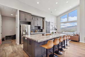 Kitchen with stainless steel refrigerator with ice dispenser, a kitchen island, light stone counters, light wood finished floors, and recessed lighting