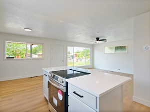Kitchen featuring stainless steel range with electric cooktop, a ceiling fan, a textured ceiling, plenty of natural light, and white cabinetry