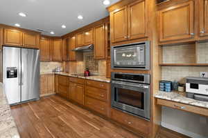 Kitchen featuring appliances with stainless steel finishes, decorative backsplash, dark wood finished floors, brown cabinetry, and recessed lighting