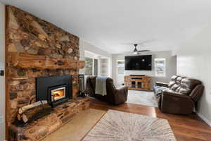 Living room featuring a stone fireplace, wood finished floors, and ceiling fan