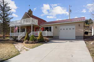View of front facade featuring a porch, an attached garage, a metal roof, and a balcony