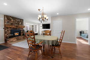 Dining space with wood finished floors, a chandelier, a stone fireplace, and recessed lighting