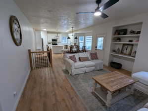 Living area featuring light wood-style flooring, a ceiling fan, a textured ceiling, and built in features
