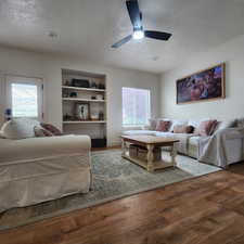 Living room with a textured ceiling, wood finished floors, built in shelves, and ceiling fan
