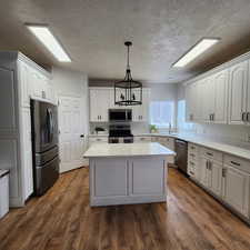 Kitchen with appliances with stainless steel finishes, a center island, white cabinets, light countertops, and dark wood-style floors