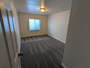 Unfurnished room featuring a textured ceiling and dark colored carpet