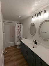 Full bath with a textured ceiling, wood finished floors, vanity, and shower / bathtub combination with curtain