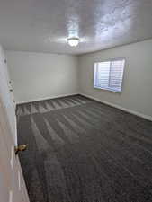 Unfurnished room featuring dark carpet and a textured ceiling