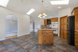 Kitchen featuring a chandelier, a skylight, arched walkways, brown cabinetry, and white appliances