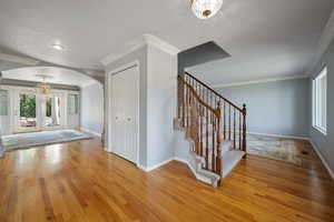Entrance foyer with arched walkways, light wood finished floors, stairs, crown molding, and a chandelier