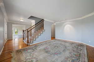 Entryway with crown molding, wood finished floors, stairway, and arched walkways