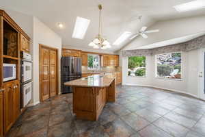 Kitchen featuring a skylight, a center island, lofted ceiling, white appliances, and light stone counters