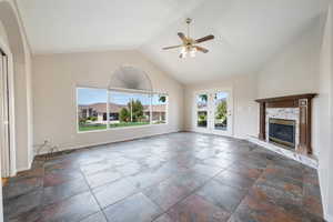 Unfurnished living room featuring ceiling fan, vaulted ceiling, and a fireplace