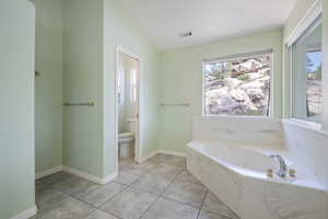 Full bathroom with healthy amount of natural light, a bath, tile patterned floors, and lofted ceiling
