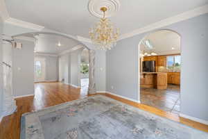 Unfurnished room featuring arched walkways, light wood finished floors, ornamental molding, and a chandelier