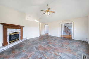 Unfurnished living room featuring ceiling fan, stone finish flooring, arched walkways, vaulted ceiling, and stairs