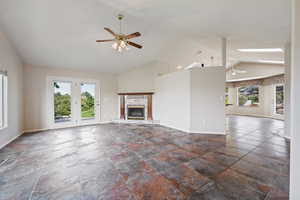 Unfurnished living room featuring ceiling fan, vaulted ceiling, and a glass covered fireplace