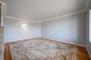 Unfurnished room featuring wood finished floors, ornamental molding, and a textured ceiling