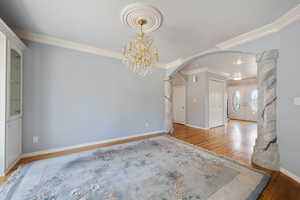Unfurnished room with wood finished floors, arched walkways, ornamental molding, a chandelier, and french doors