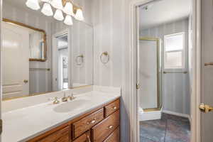 Full bath with a shower stall, vanity, stone finish flooring, and wallpapered walls