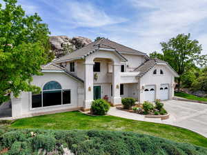 View of front of house with driveway, stucco siding, a tile roof, a front yard, and an attached garage