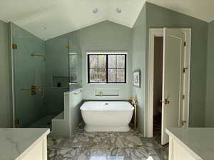 Primary bathroom with 2 vanities, vaulted ceiling, a freestanding bath, a shower stall, and marble flooring