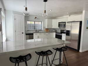 Kitchen with appliances with stainless steel finishes, a textured ceiling, dark wood finished floors, a kitchen bar, and white cabinetry